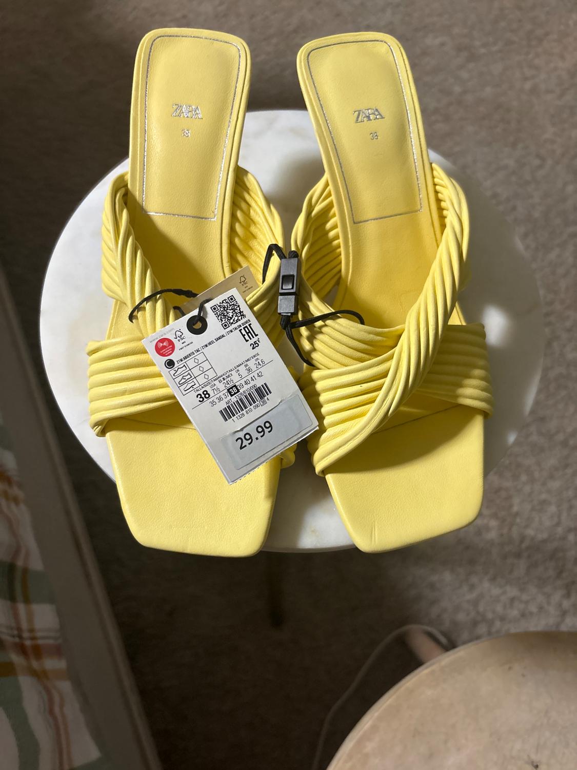 Low-heeled yellow sandals with a braided design, price tag of 29.99, on a white table.