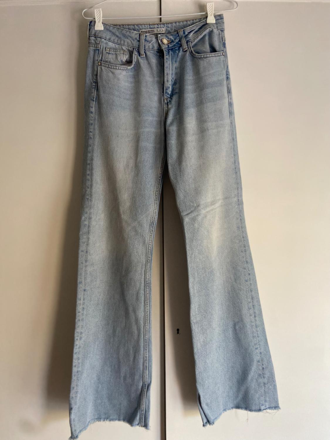 Light blue denim jeans with a frayed hem, hanging on a white hanger against a neutral background.