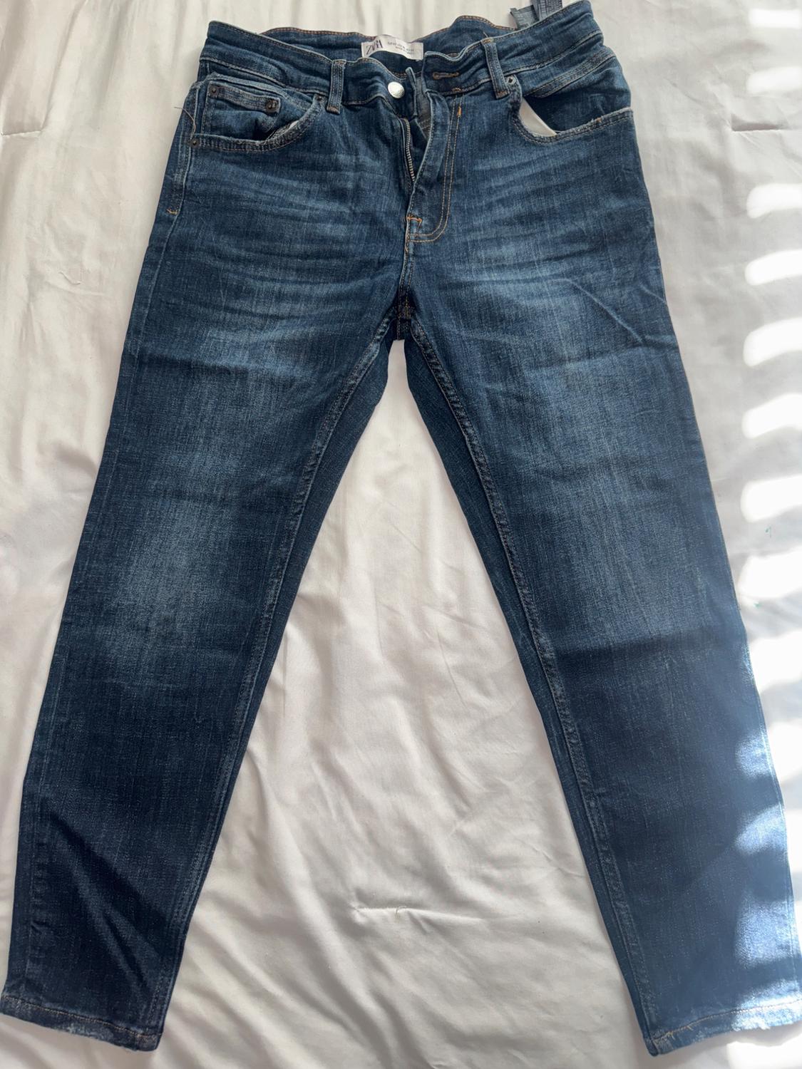 Dark blue jeans on a white surface, with visible stitching details and a metallic button closure.