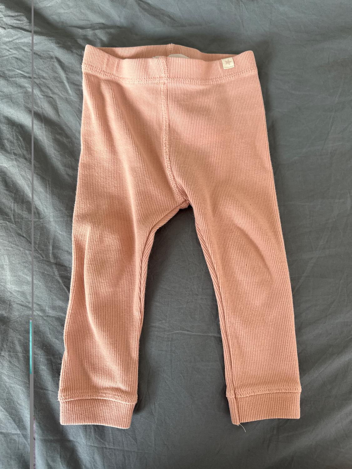 Light pink baby trousers with a ribbed texture, placed on a grey surface. Small label visible on the waistband.
