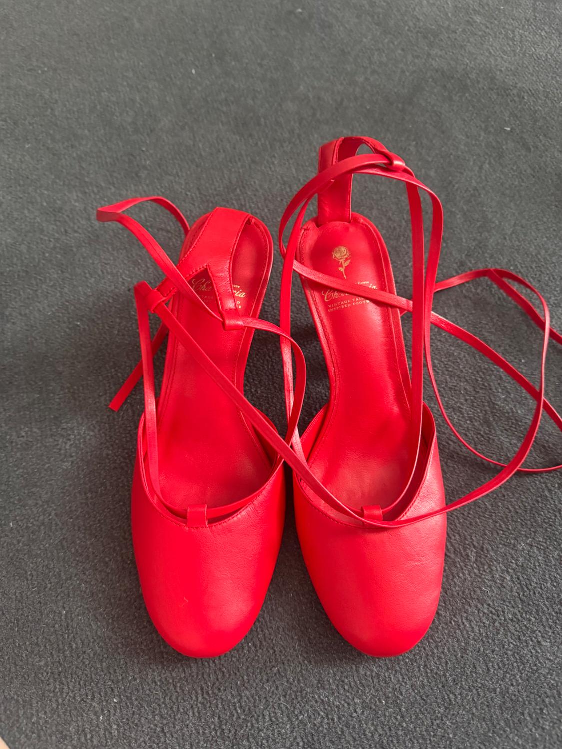 Red high-heeled shoes with long straps to tie at the ankle, seen from above on a textured grey background.