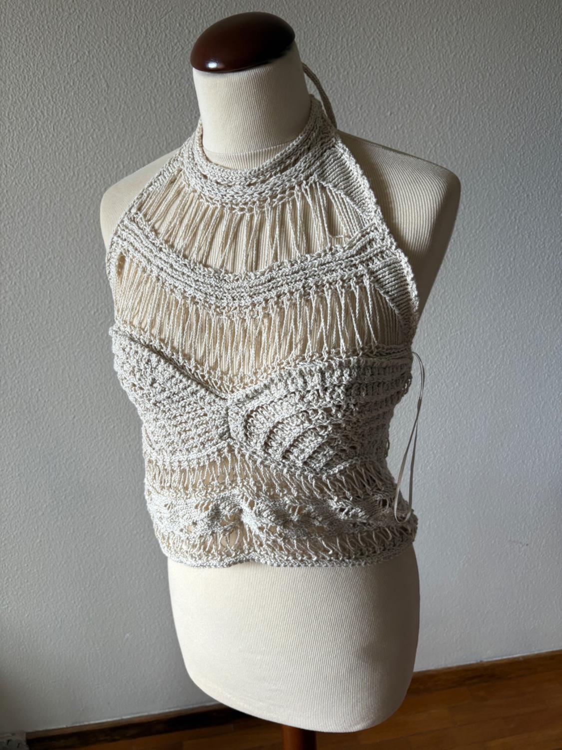 Mannequin wearing a beige open-knit halter neck top with textures. Light wall and wooden floor background. Bohemian and relaxed style.