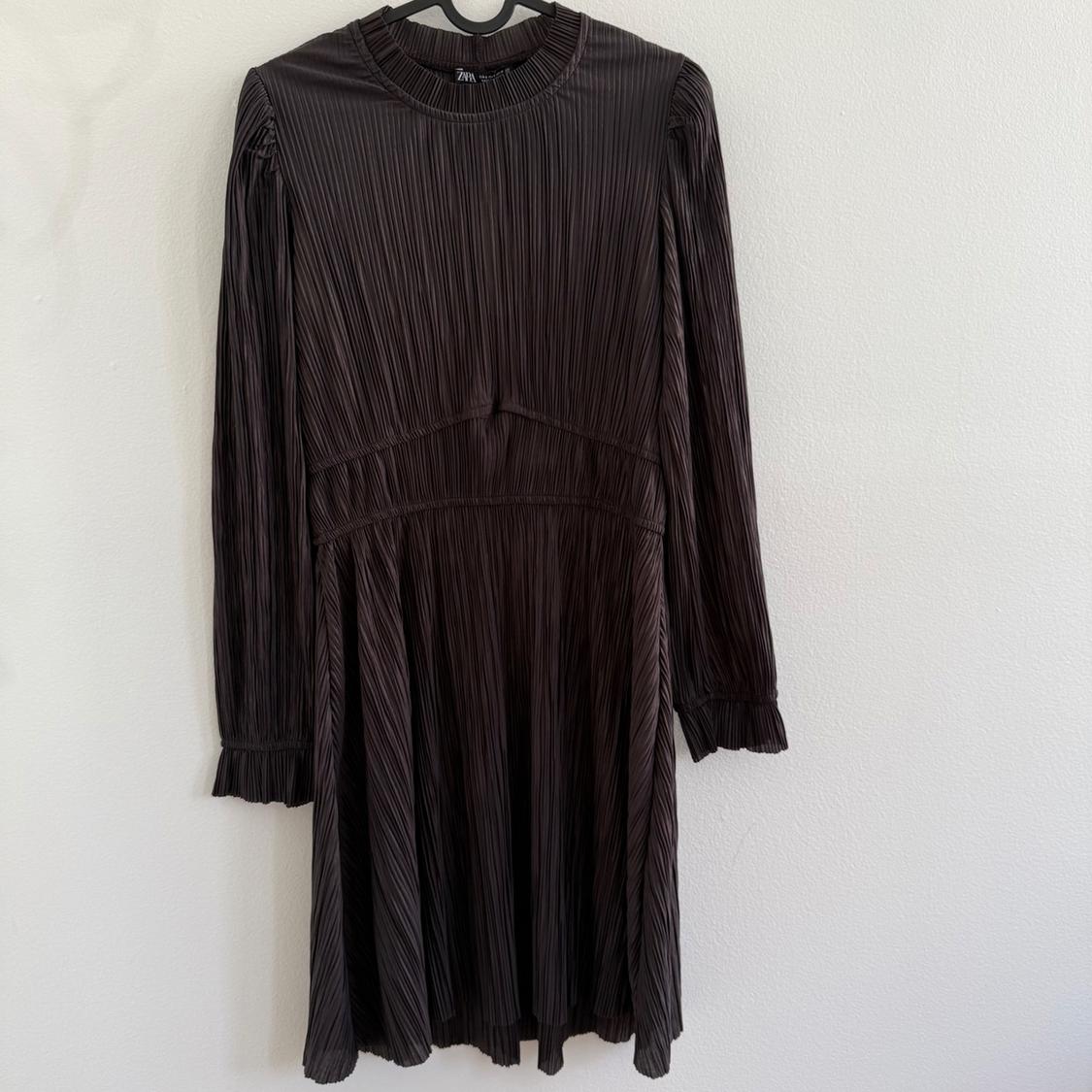 Pleated black long-sleeve dress with a round neck, gathered details at the cuffs, and a waist cut, hanging on a hanger.