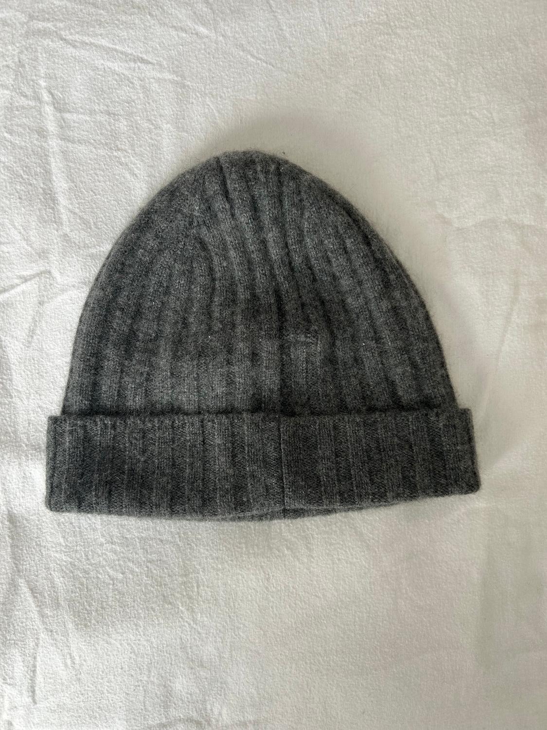 Grey knitted hat on a white background, with a ribbed design and folded brim.