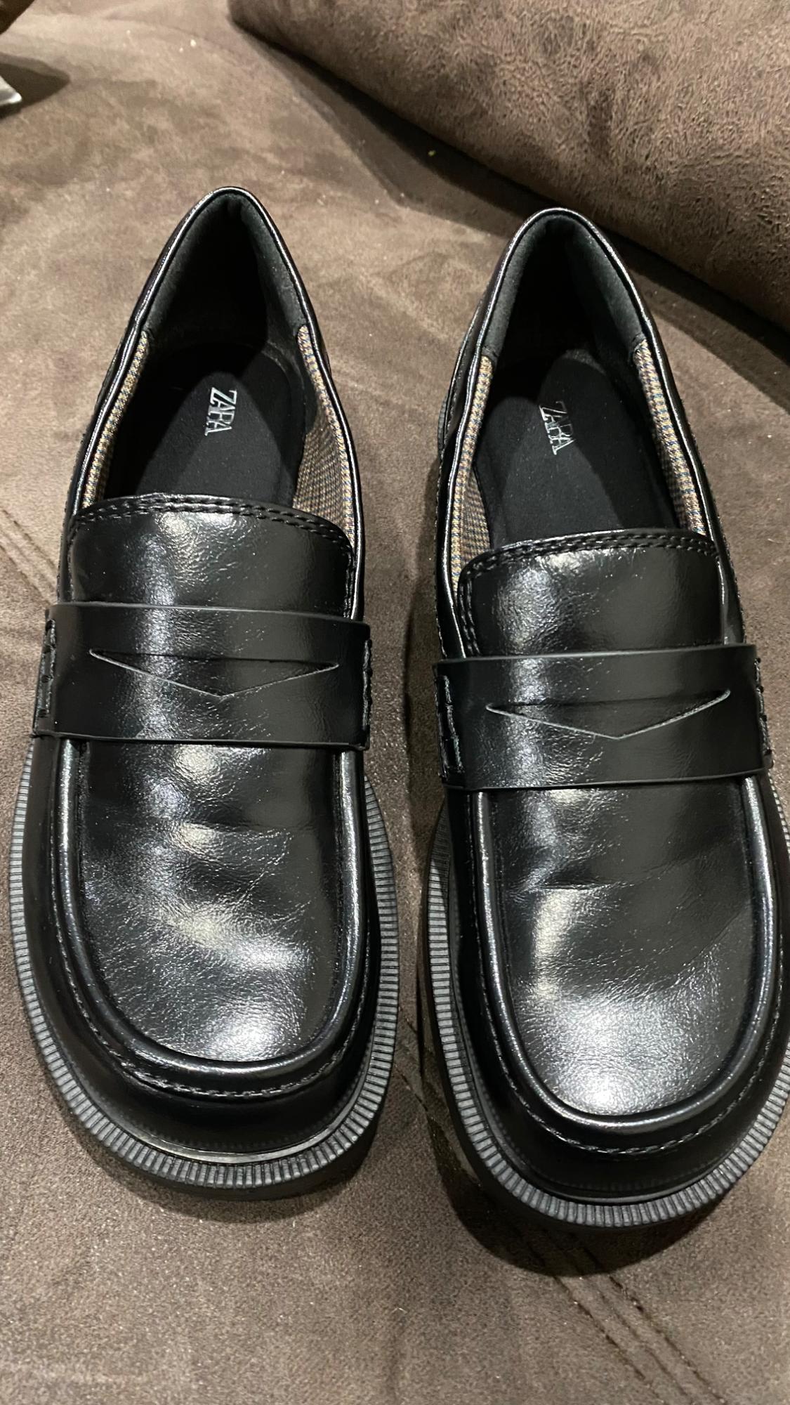 Black patent leather shoes with a chunky sole on a brown surface. The inside shows the brand "ZARA".