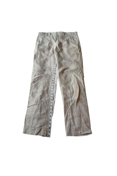 Beige linen trousers on a white background. A numbered measuring tape is extended along the left leg.