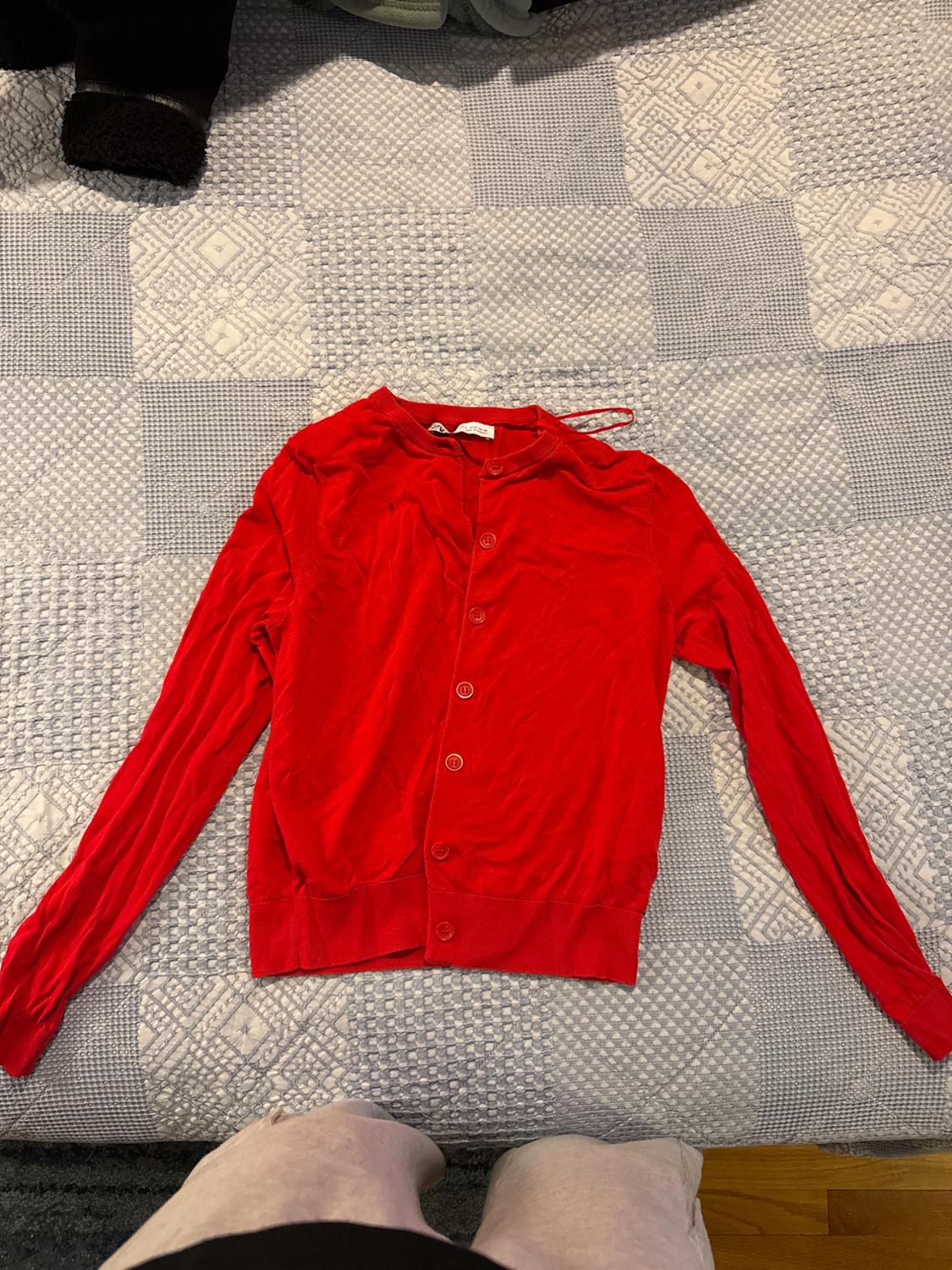 Red long-sleeved cardigan with buttons, spread out on a geometric patterned comforter in shades of gray and white.