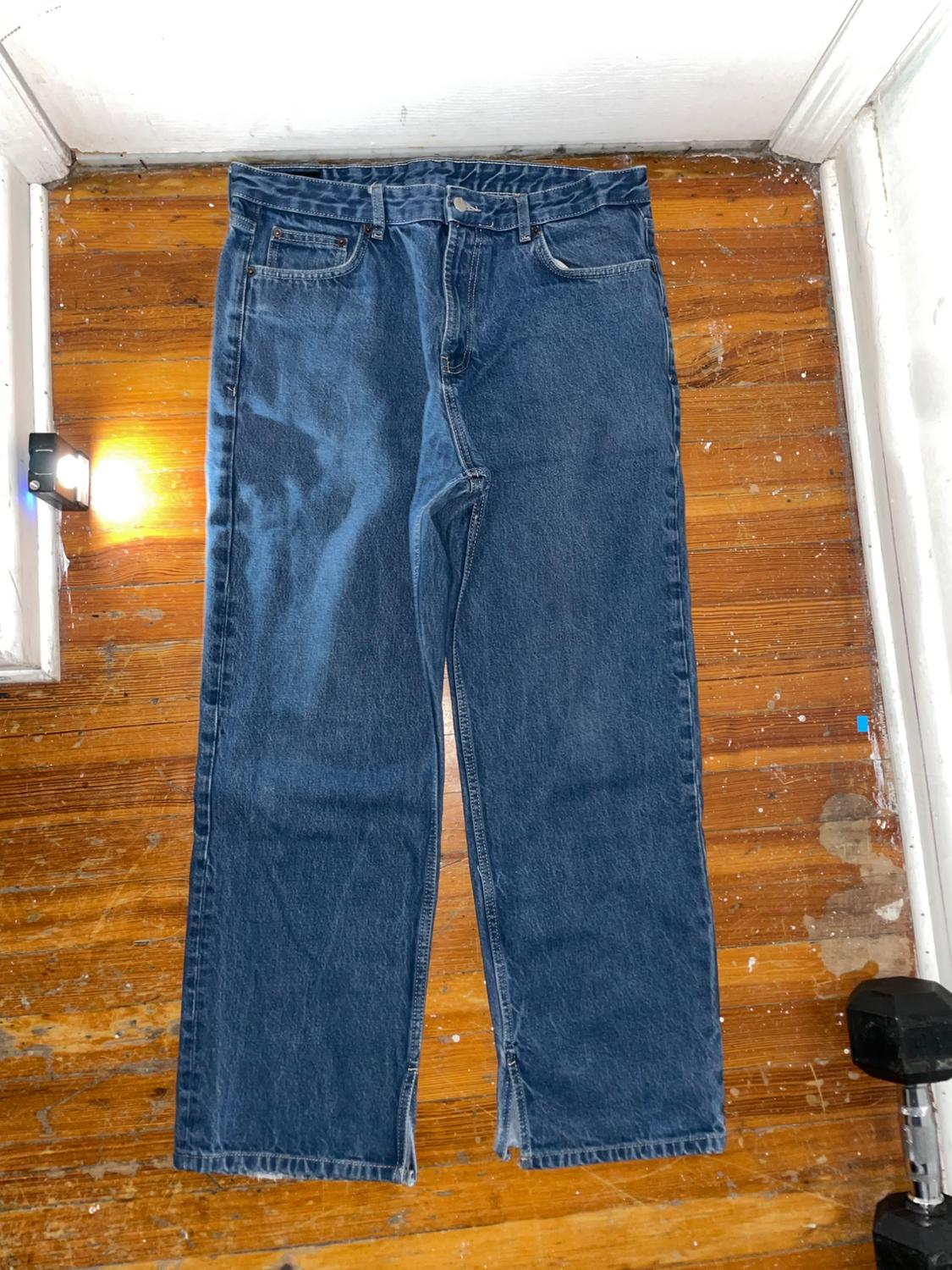 Blue straight-leg jeans laid out on a wooden floor. A casual-style composition with a spotlight on the left side.