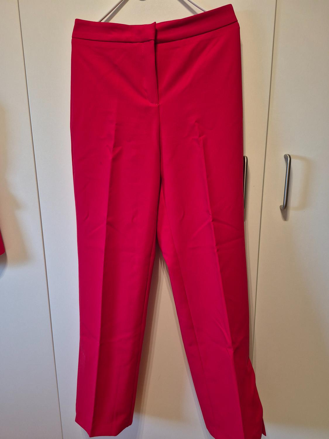 Fuchsia suit trousers with a pressed crease, hanging on a hanger in front of a white wardrobe.