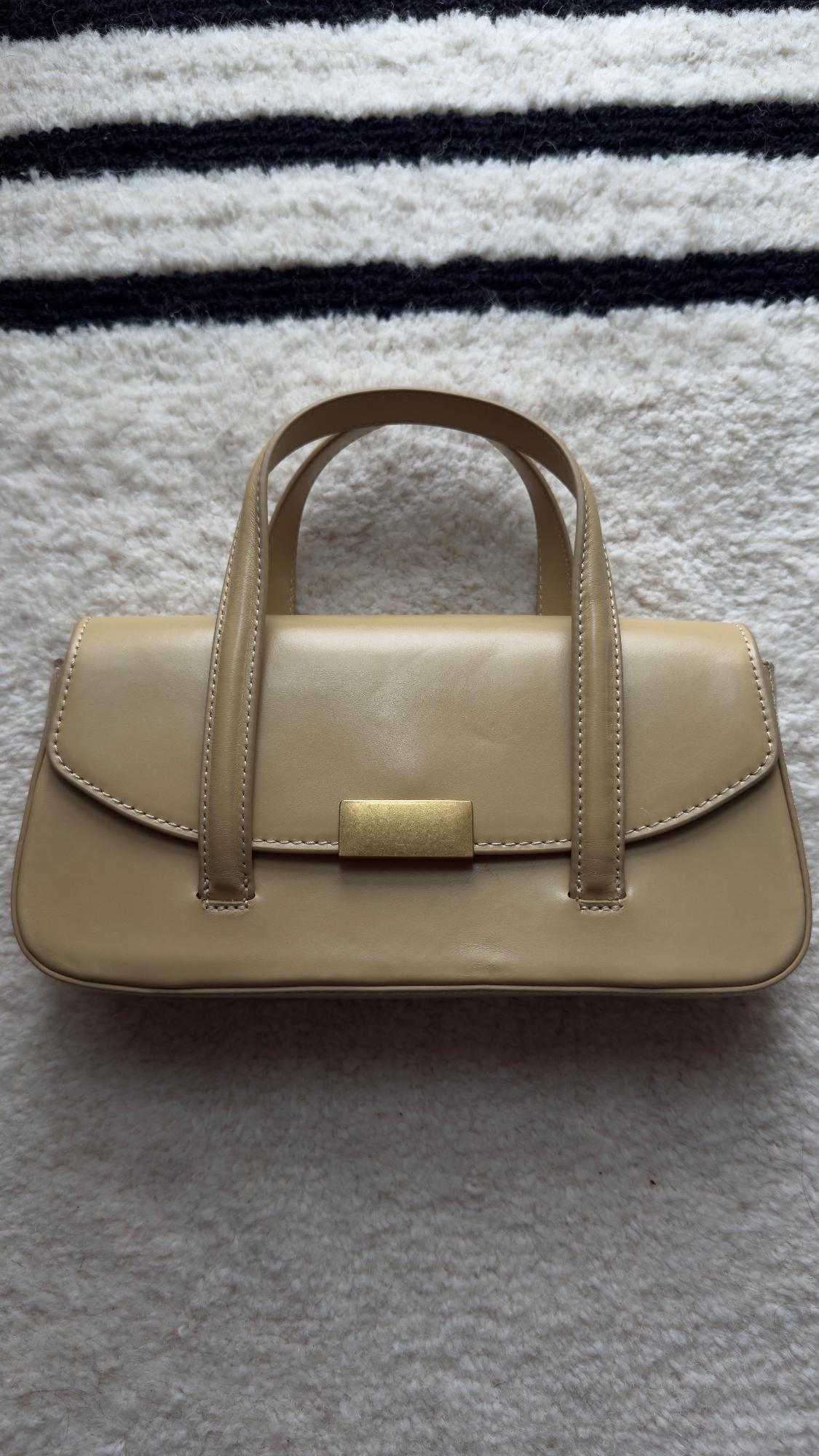 Beige leather handbag with gold clasp on a black and white striped rug. Elegant and minimalist design.