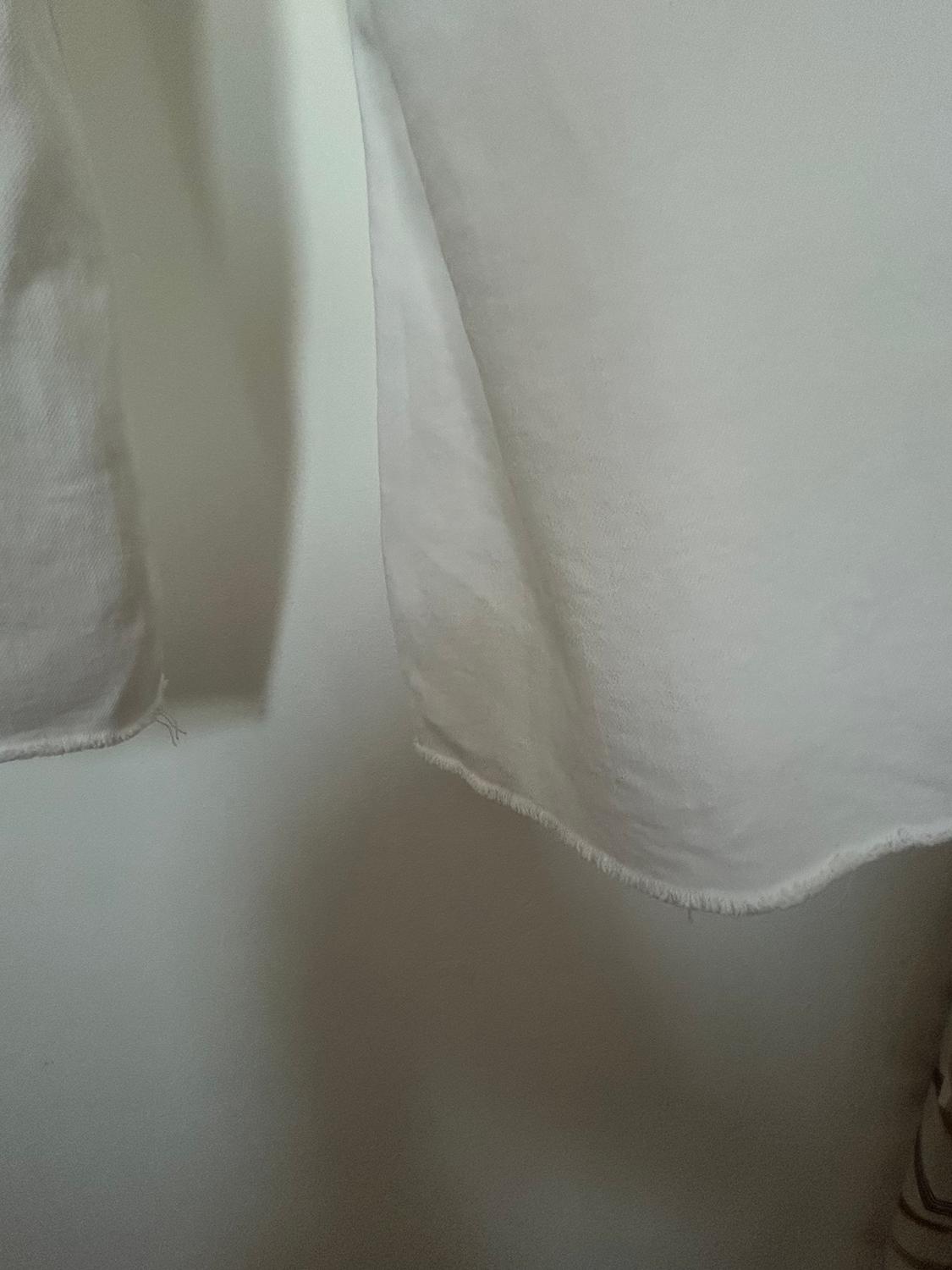 White fabric with frayed edges hanging, creating soft shadows on a light-coloured wall.