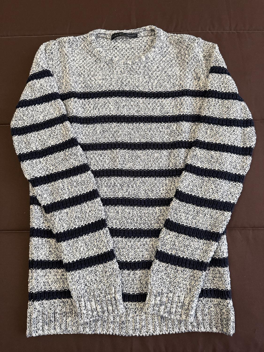 Grey knitted jumper with black horizontal stripes on a brown background. Classic design and thick texture.