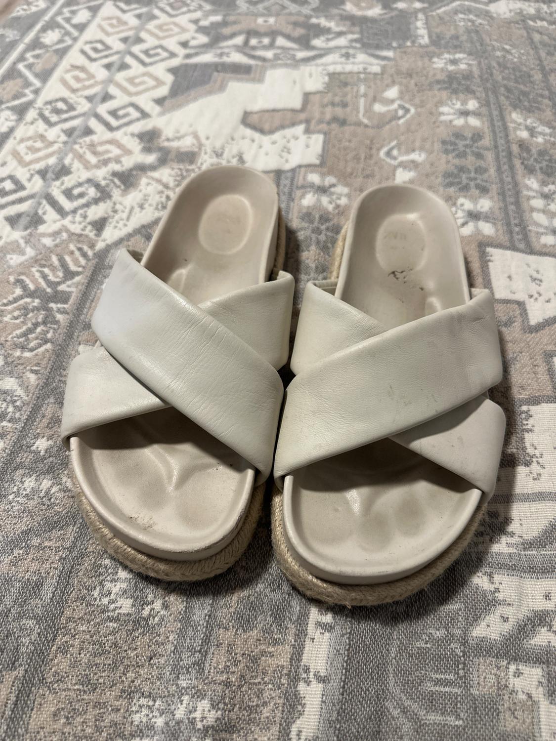 White sandals with crossed straps on a geometric design rug in beige and grey tones.