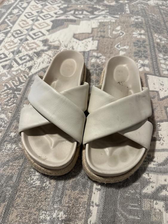 White sandals with crossed straps on a geometric design rug in beige and gray tones.
