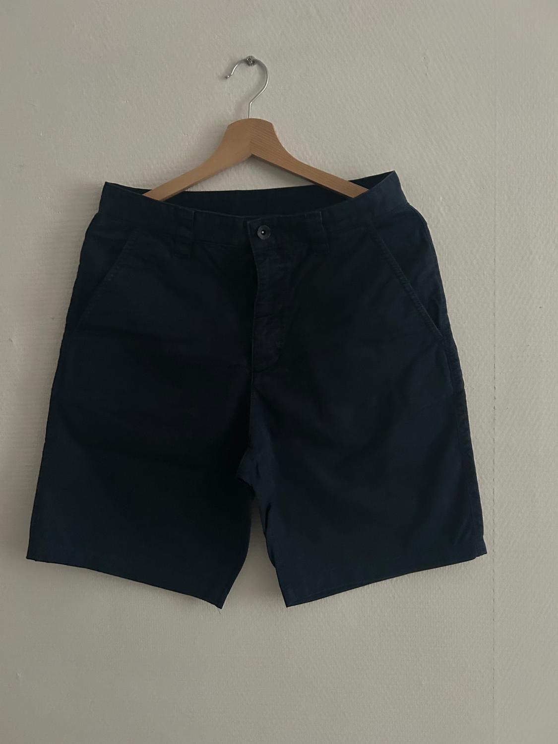 Dark shorts hanging on a wooden hanger against a white wall.