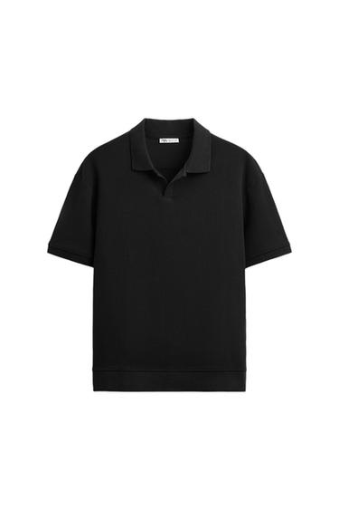 Black short-sleeve polo shirt with ribbed texture and classic collar. White background. Visible tag on the inside of the collar.