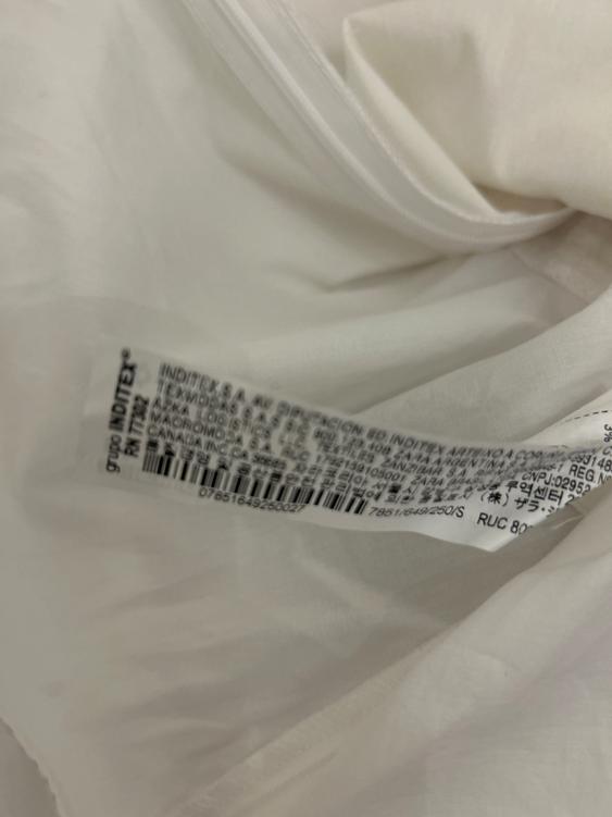 White clothing label with multi-language text and a visible barcode. The fabric is soft and slightly creased.