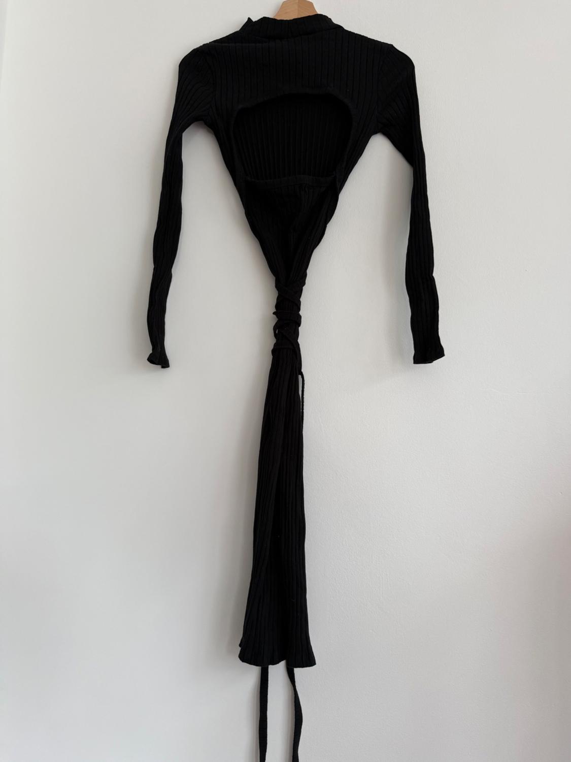 Black long-sleeved dress with a slit in the back, hanging on a hanger against a white wall.