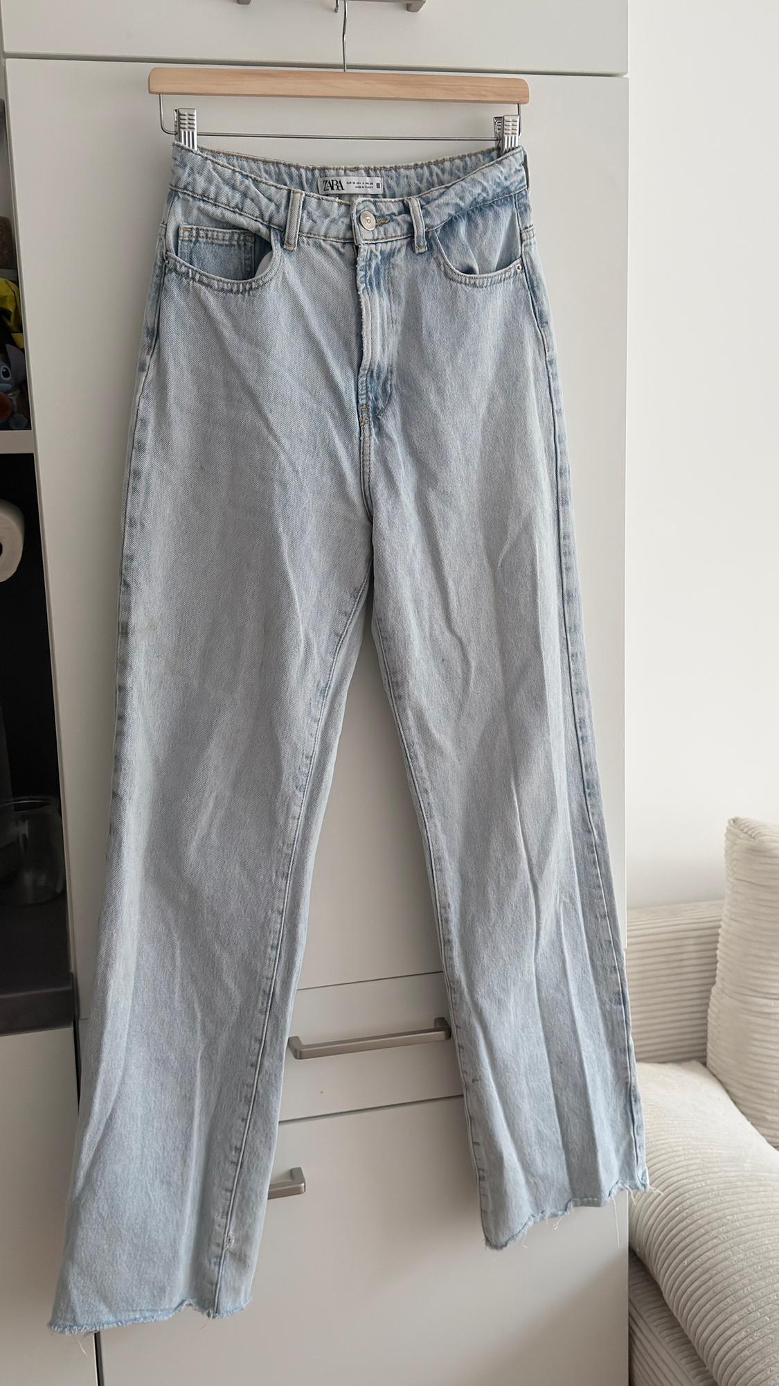 Light blue denim jeans hanging on a wooden hanger in front of a white wardrobe.