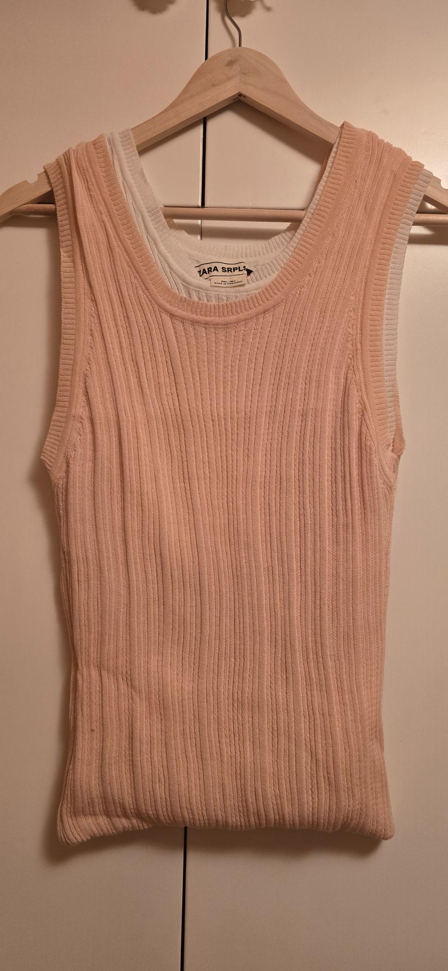 Sleeveless light pink ribbed knit top over a white one, hanging on a wooden hanger. Visible text: ZARA SRPLS.
