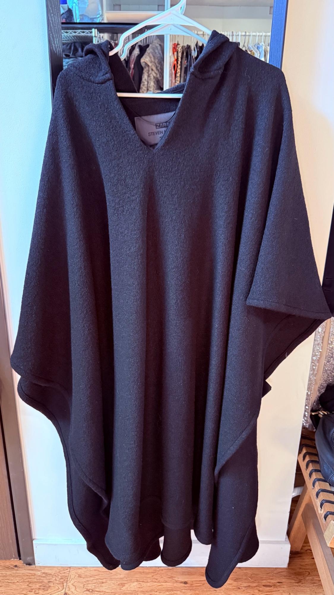 Black hooded poncho hanging on a hanger in front of a mirror reflecting a closet. Interior label with the text ZARA STEVEN M.