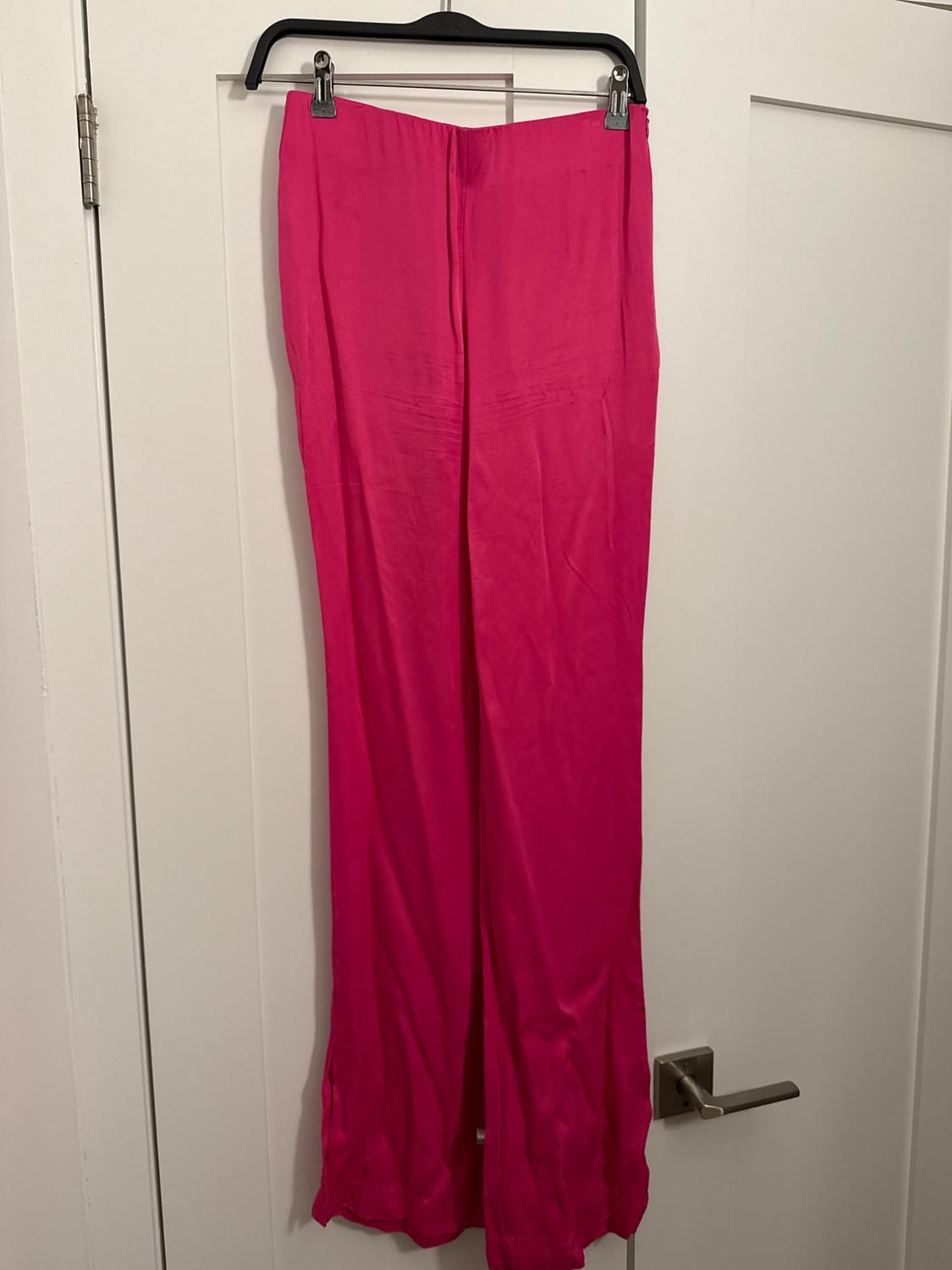 Bright pink long pants hanging on a black hanger over a white door.