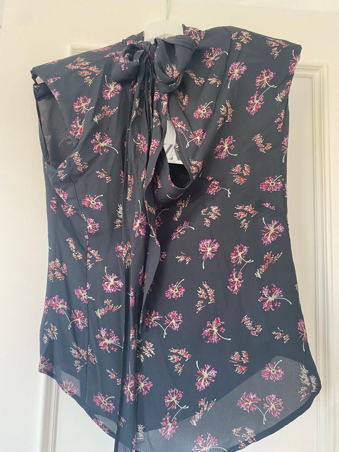 Sleeveless hung blouse, with a floral print in pink and purple tones on a black background, with a bow at the neck.