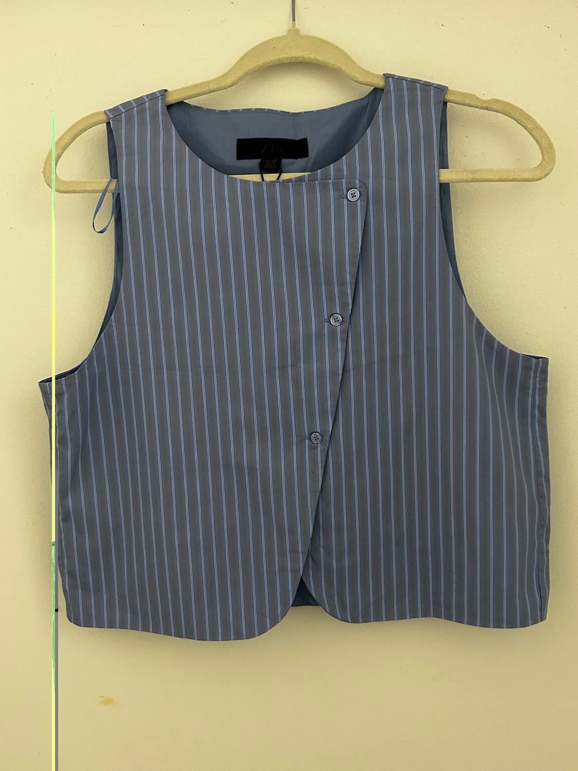 Blue and gray striped sleeveless vest hanging on a beige hanger against a light background.