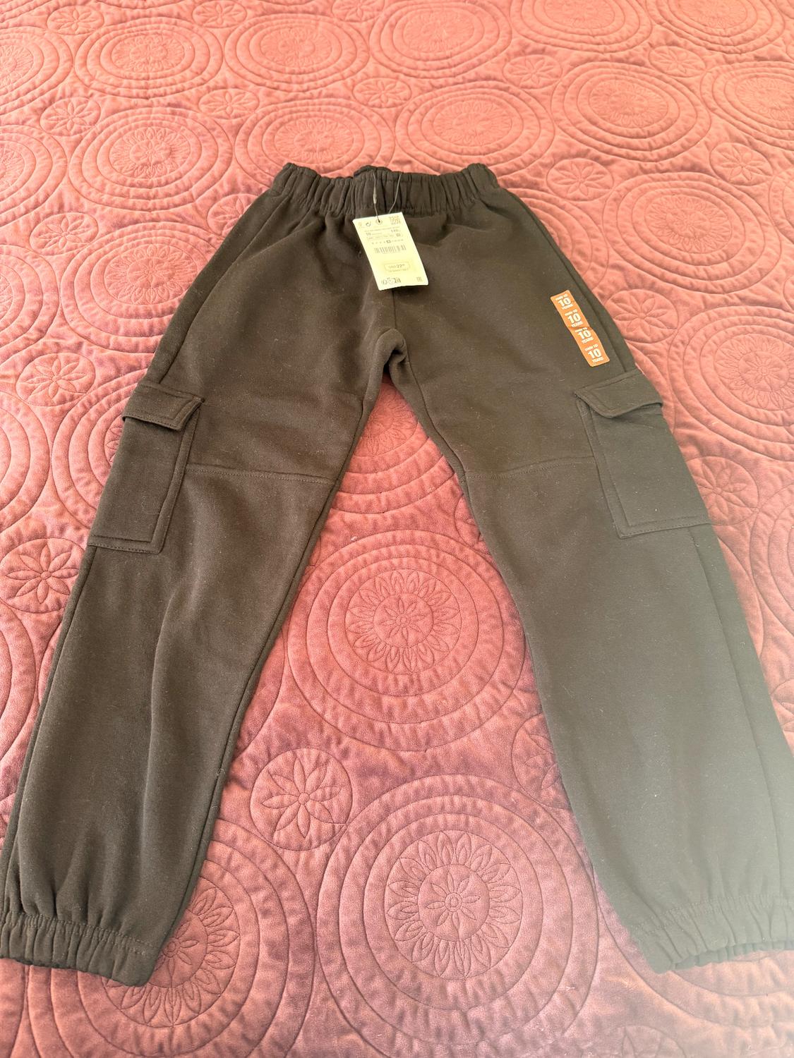 Black cargo pants with side pockets and a tag on the waist, on a pink comforter with a circular design.