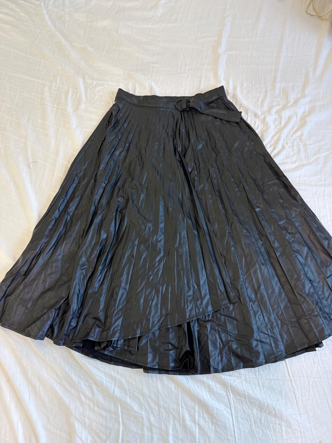 Pleated black skirt with a belt, laid flat on a white surface. Shiny fabric and wrinkled texture visible.