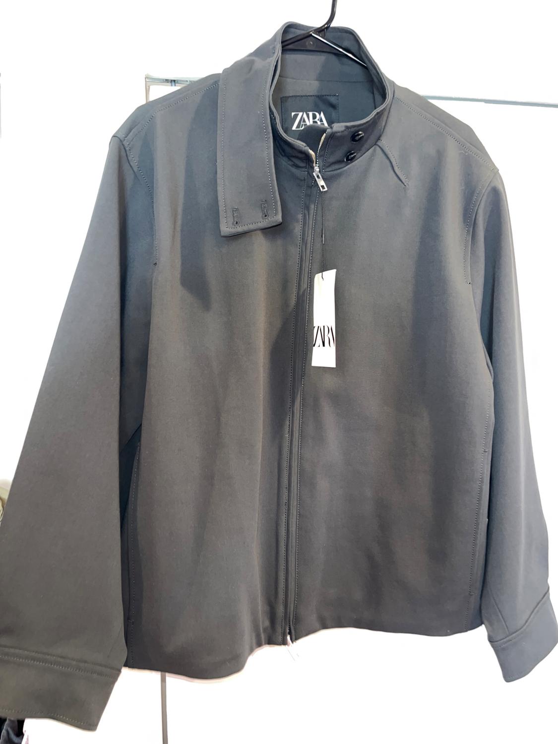 Black zip-up, high-neck jacket hanging on a hanger. Visible label with the text "ZARA". White background.