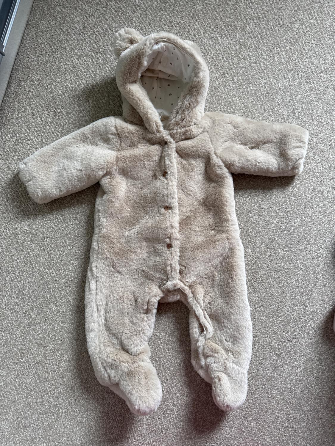 Beige plush baby all-in-one with hood and ears, on a grey rug. Inside with small star print.