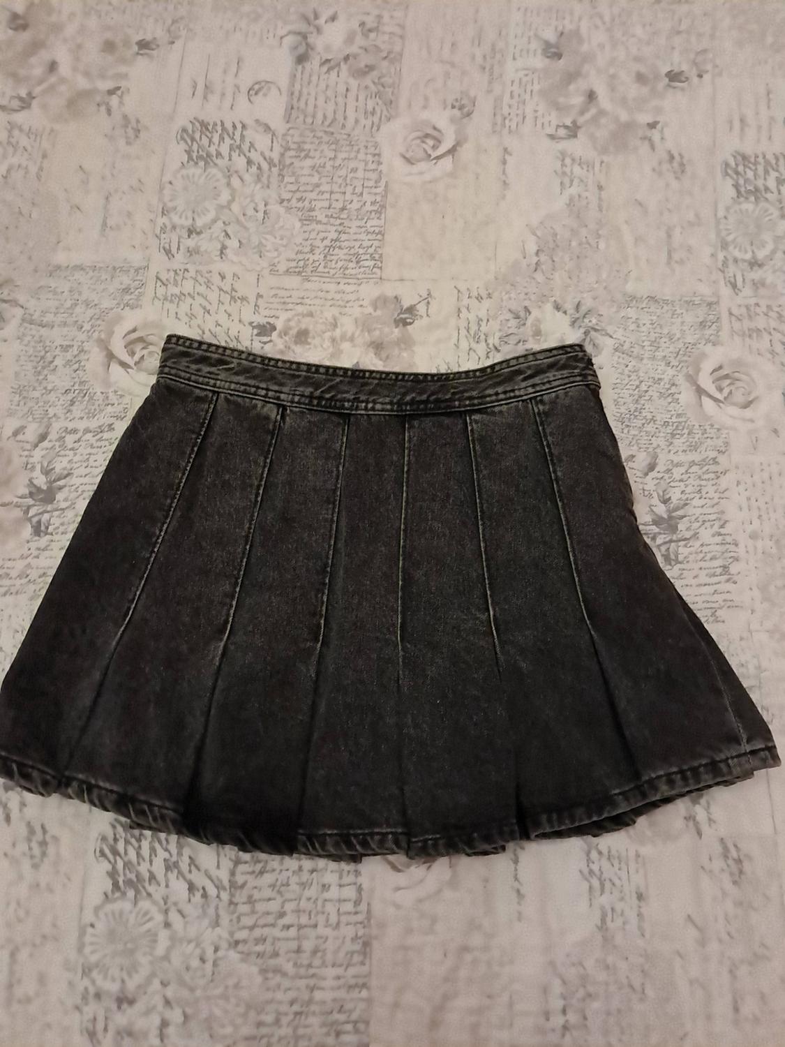 Black pleated denim miniskirt on a surface featuring a text and rose print.