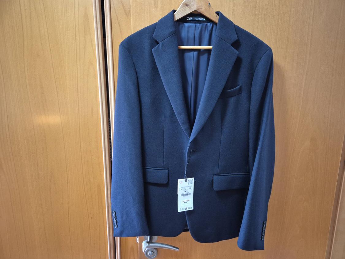 Navy blue jacket hanging on a wooden door, with a visible label. Simple and elegant atmosphere.