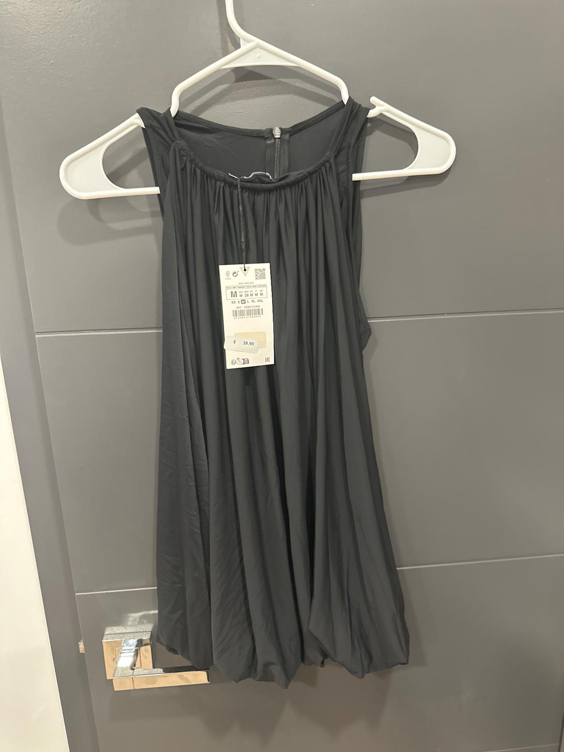 Sleeveless black dress hanging on a white hanger against a gray wall. Visible tag with a price of 39.90.