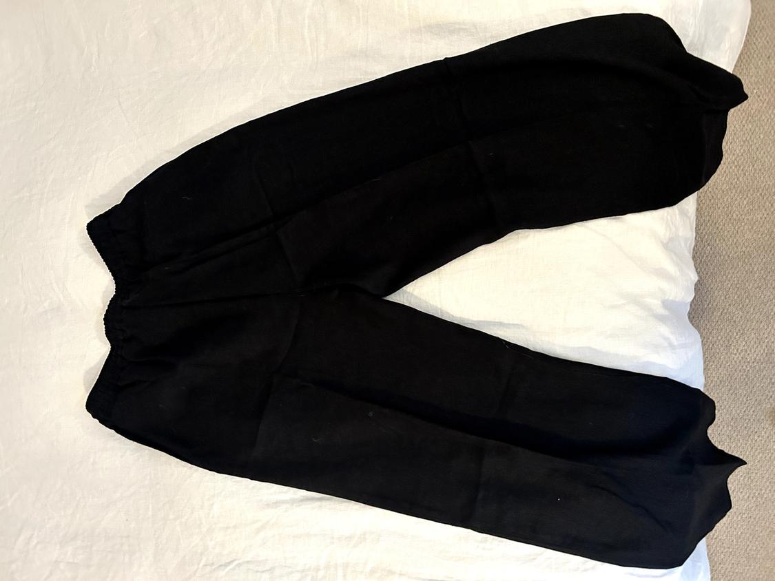Black soft fabric trousers with an elasticated waist, placed on a white surface.