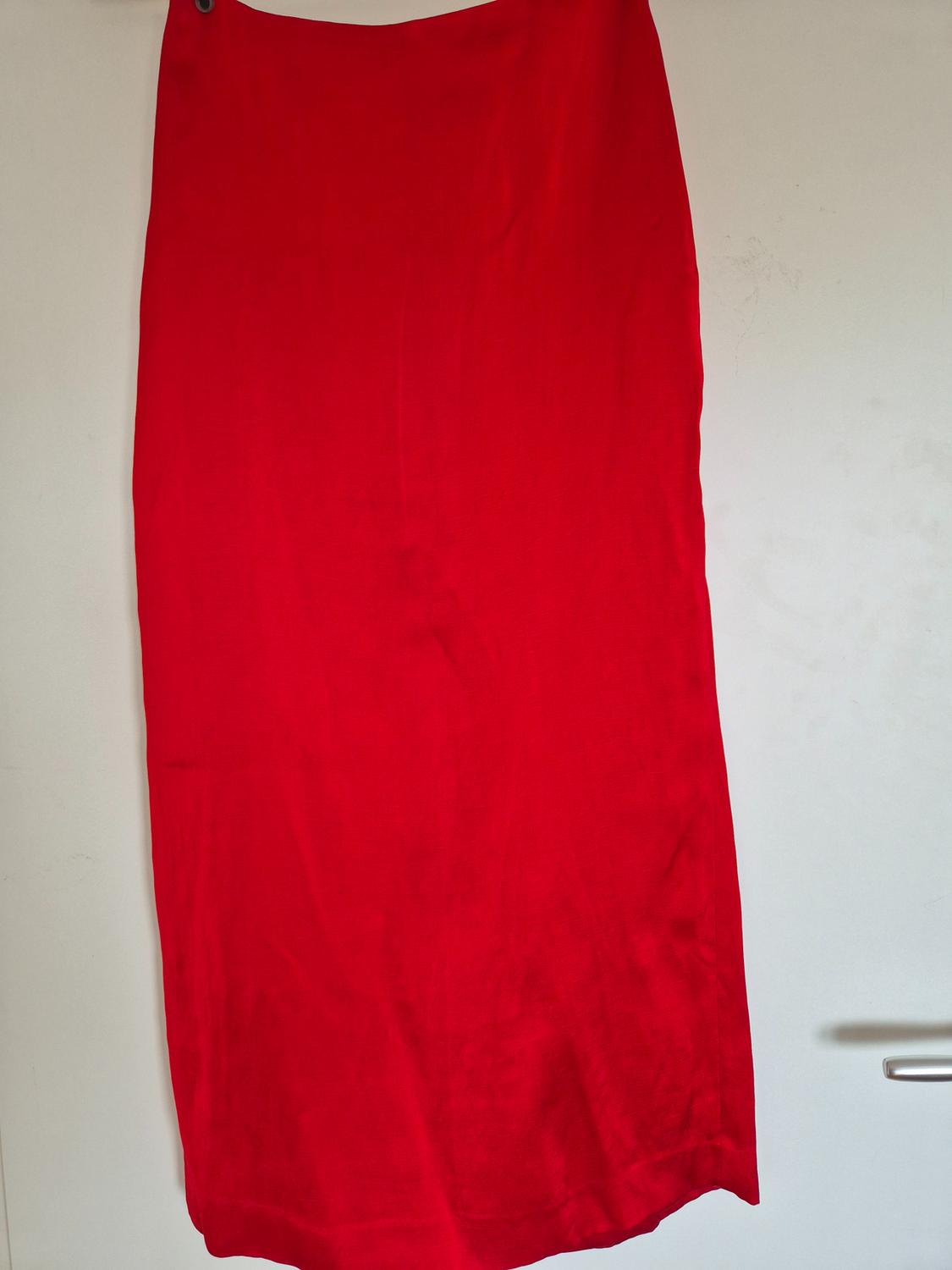 Long red skirt hanging against a white wall, showing its smooth texture and straight drape.