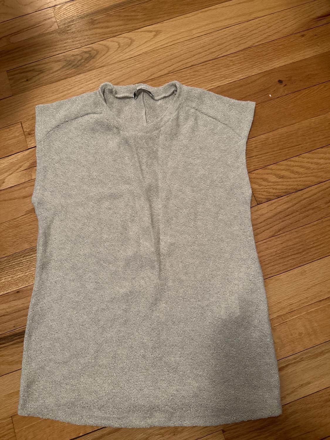 Light gray sleeveless t-shirt on wooden floor. Knit fabric with a round neckline and seam detail on the shoulders.