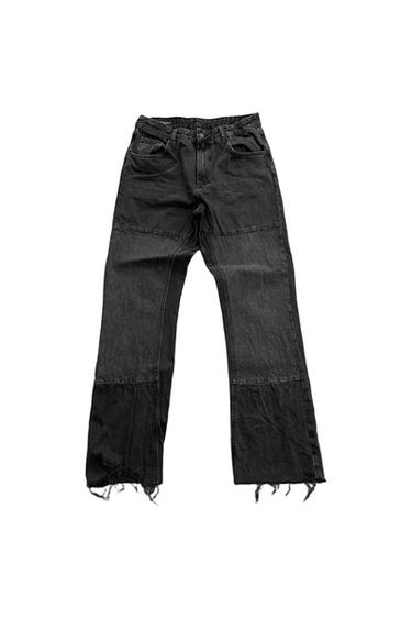 Distressed black denim pants with panels, horizontal stitching, and a frayed hem, on a white background.