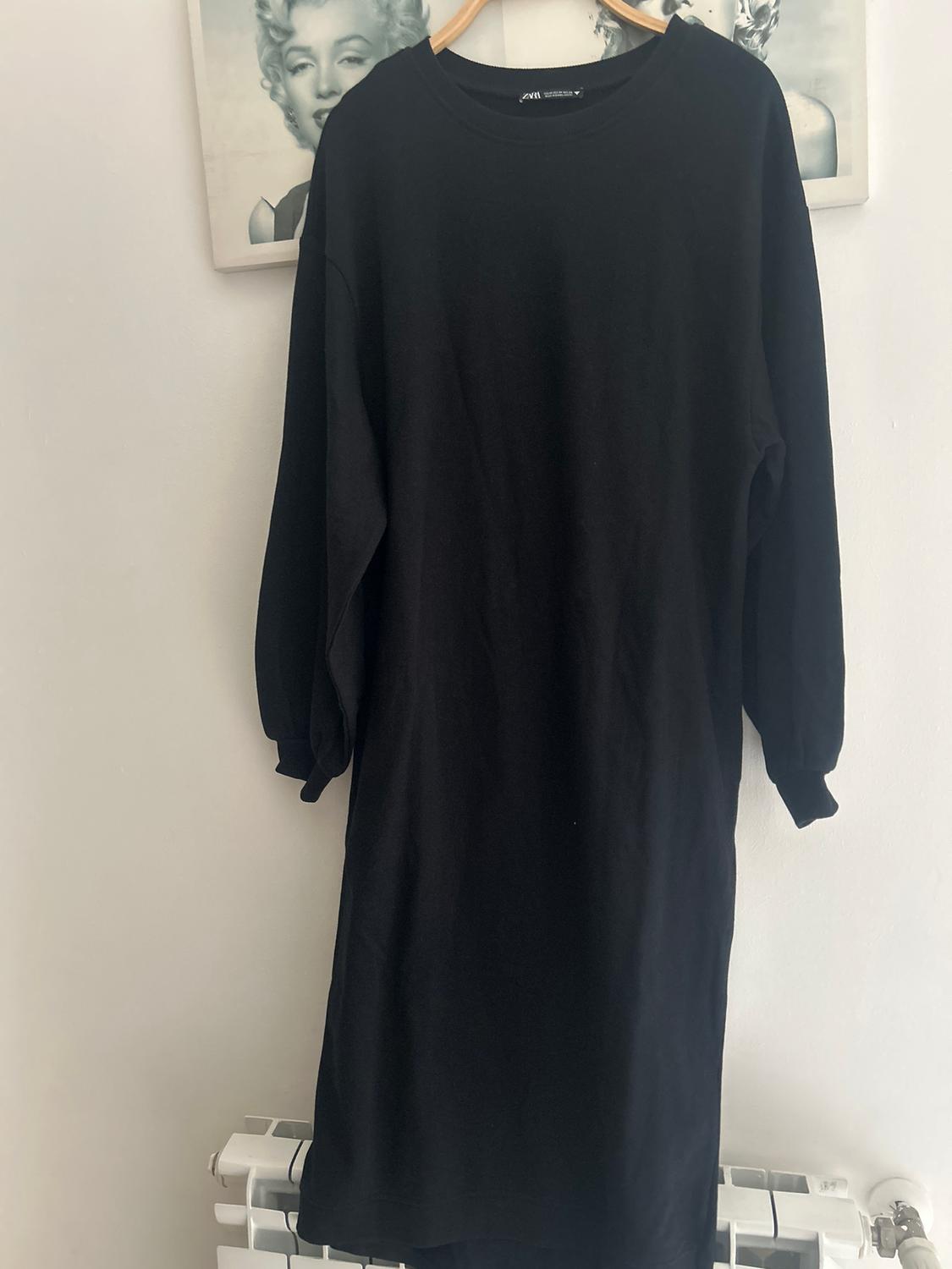 Black long-sleeved dress hanging on a hanger against a background of black and white photos.