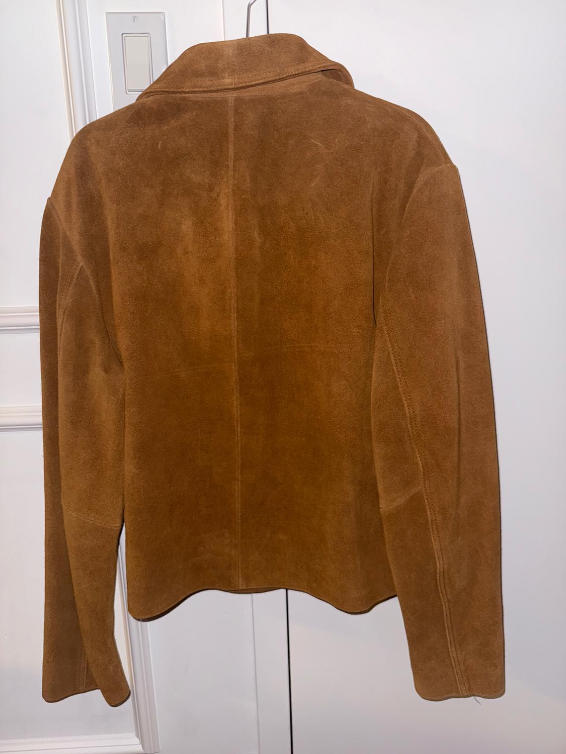 Brown suede jacket seen from the back, hanging on a hanger in front of a white door with a visible light switch on the left.