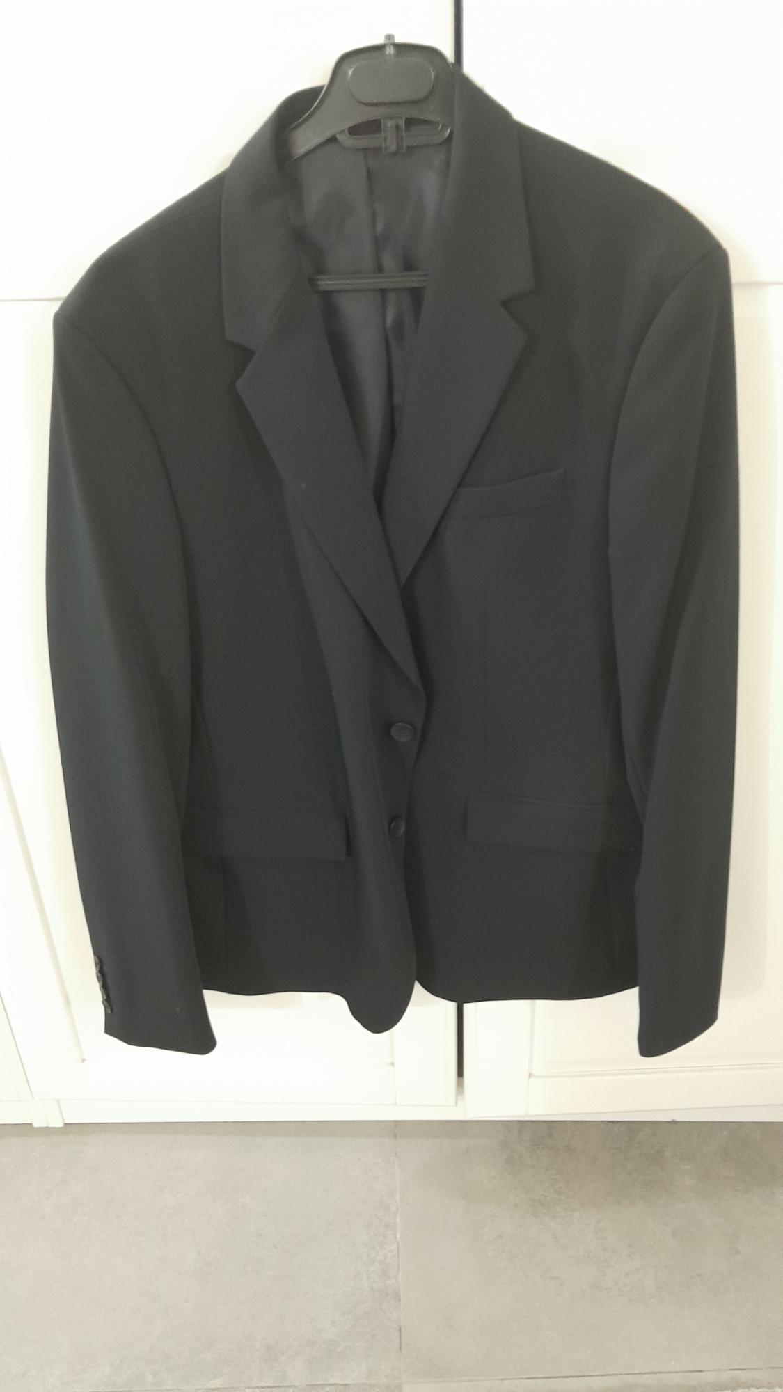 Black suit jacket hanging on a black hanger, against a background of white doors and a grey floor.