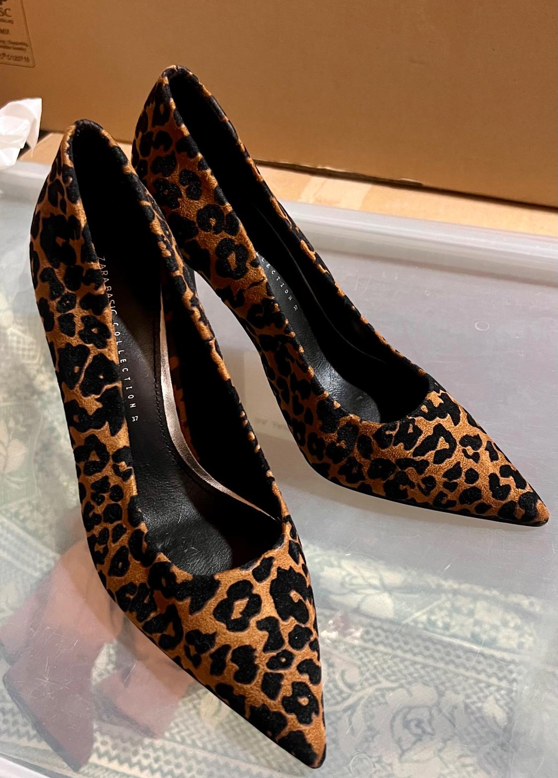 Leopard print high heels in brown and black tones on a light surface. Visible text: "ZARA BASIC COLLECTION".