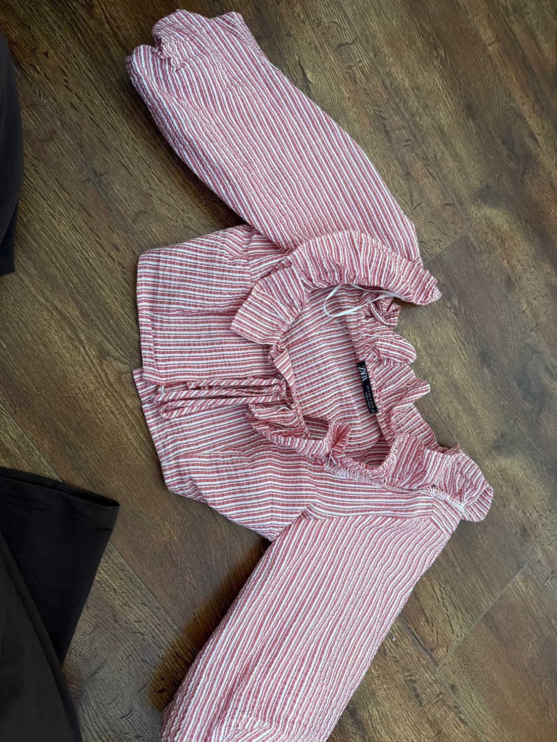 Red and white striped blouse with ruffles on the sleeves and collar, on a dark wooden floor.