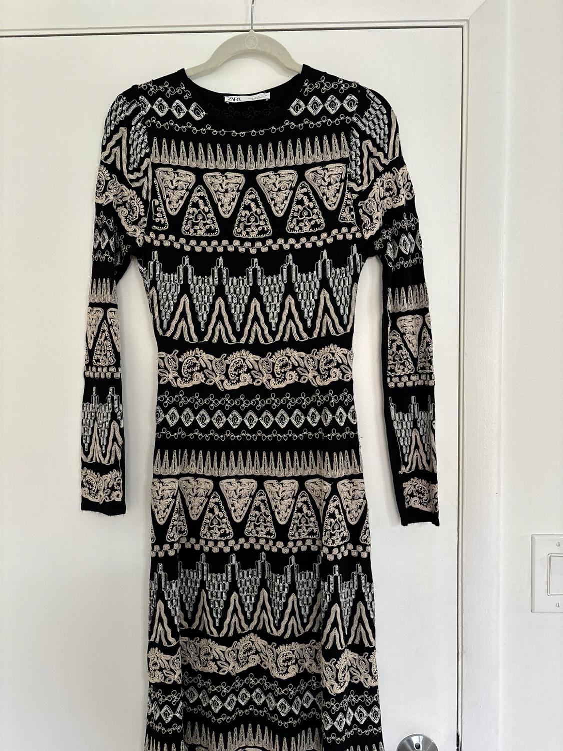 Long-sleeved black ZARA dress with light geometric patterns, hanging on a hanger on a white door.