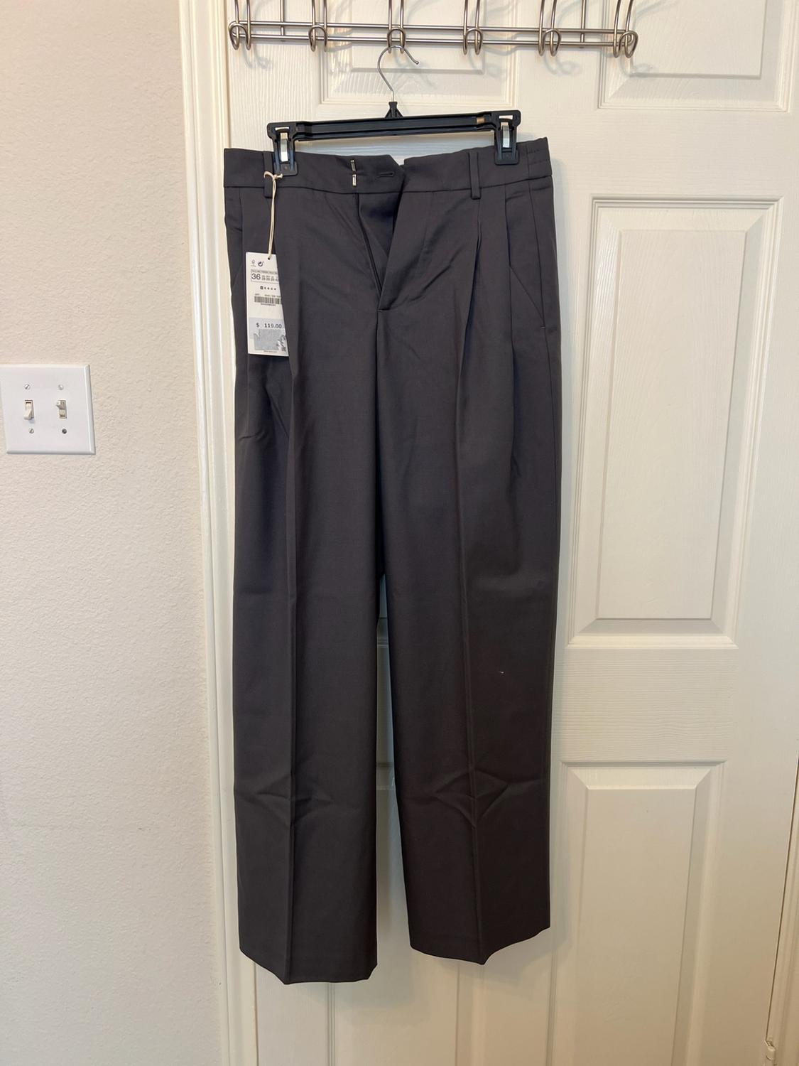 Dark grey formal trousers with pleats hanging on a white door. Visible label with the text "36" and "$119.00".