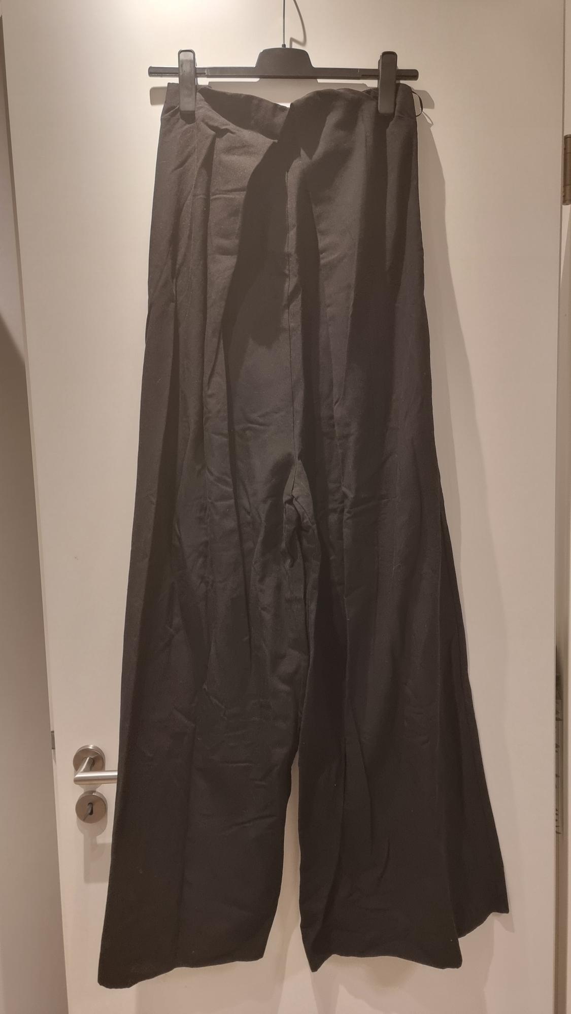 Black wide-leg trousers hanging on a hanger over a white door. The fabric has a wrinkled appearance.