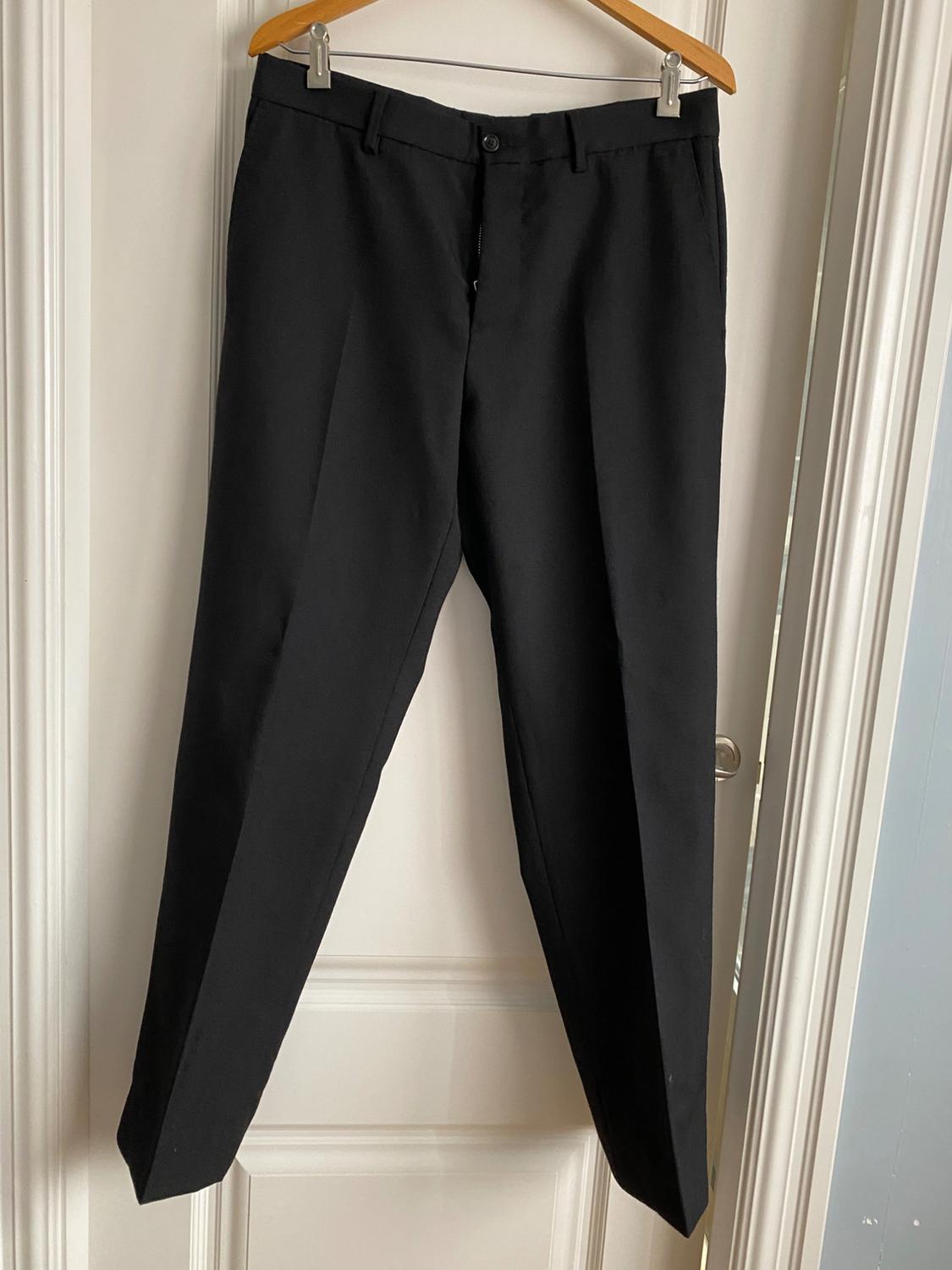 Black dress trousers hanging on a wooden hanger over a white door.