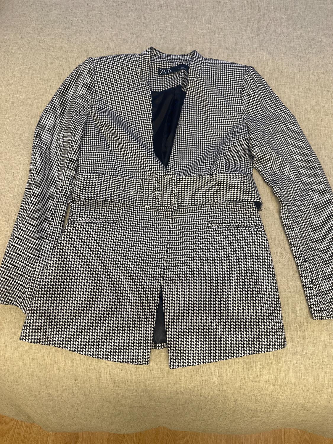 Black and white checked jacket with belt, on a beige surface. Visible label with text "ZARA".
