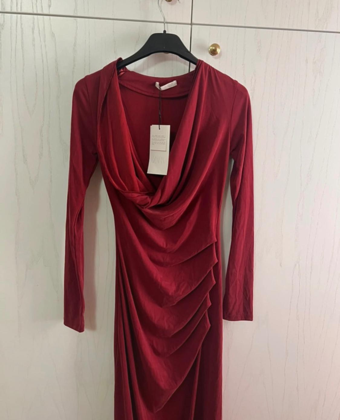 Red long-sleeved dress with a draped neckline and front pleats, hanging on a black hanger in front of a white wardrobe.